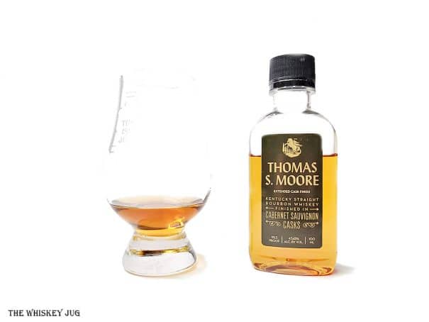 White background tasting shot with a sample bottle of the Thomas S. Moore Bourbon Cabernet Sauvignon Casks and a glass of whiskey next to it.