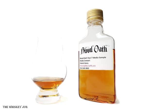 White background tasting shot with the Blood Oath Pact 7 sample bottle and a glass of whiskey next to it.