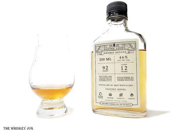 White background tasting shot with the Hooten Young Whiskey 12 Years bottle and a glass of whiskey next to it.