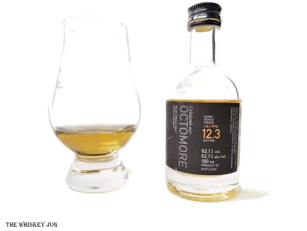 White background tasting shot with the Octomore 12.3 sample bottle and a glass of whiskey next to it.