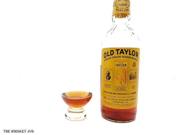White background tasting shot with the 1986 Old Taylor Bottled In Bond bottle and a glass of whiskey next to it.