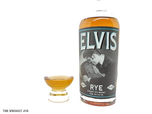 White background tasting shot with the Elvis Rye Whiskey bottle and a glass of whiskey next to it.