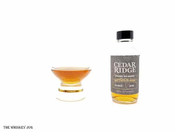 White background tasting shot with the Cedar Ridge Bottled In Bond Rye sample bottle and a glass of whiskey next to it.