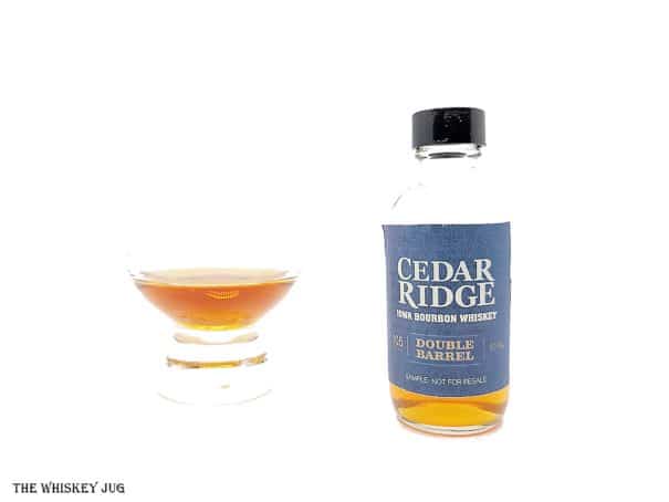 White background tasting shot with the Cedar Ridge Double Barrel Bourbon sample bottle and a glass of whiskey next to it.