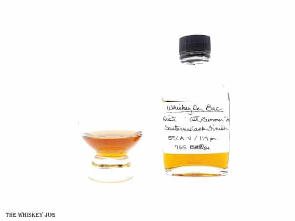 White background tasting shot with the Del Bac Distiller's Cut Summer 21 sample bottle and a glass of whiskey next to it.
