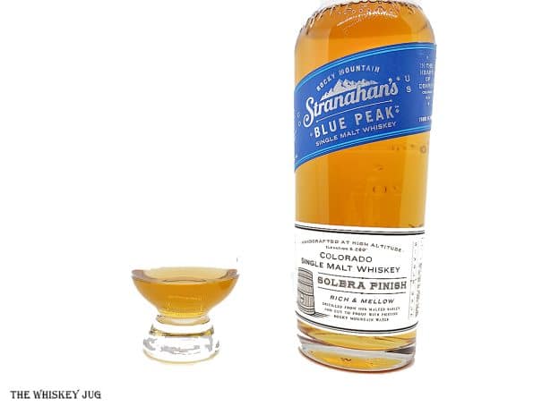 White background tasting shot with the Stranahan's Blue Peak bottle and a glass of whiskey next to it.