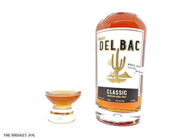 White background tasting shot with the Whiskey Del Bac Classic Single Malt bottle and a glass of whiskey next to it.