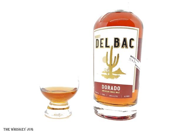 White background tasting shot with the Whiskey Del Bac Dorado bottle and a glass of whiskey next to it.