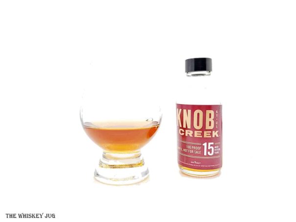 White background tasting shot with the Knob Creek 15 Years 2022 bottle and a glass of whiskey next to it.