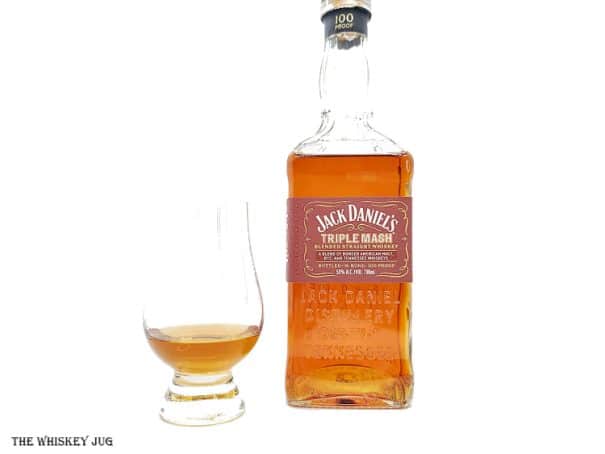 White background tasting shot with the Jack Daniel's Triple Mash Whiskey bottle and a glass of whiskey next to it.